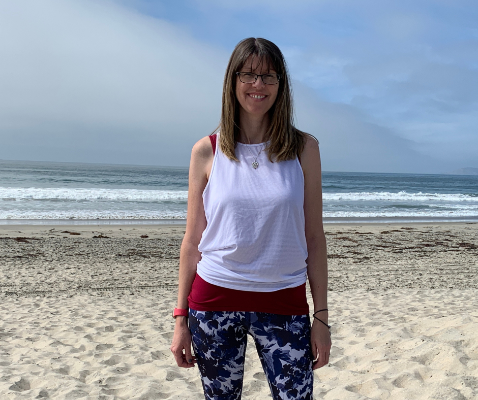 zoe standing in a white tshirt and colourful trousers on a beach
