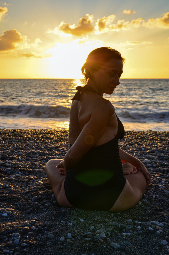 seated woman doing a yoga twist in the sunset on the beach
