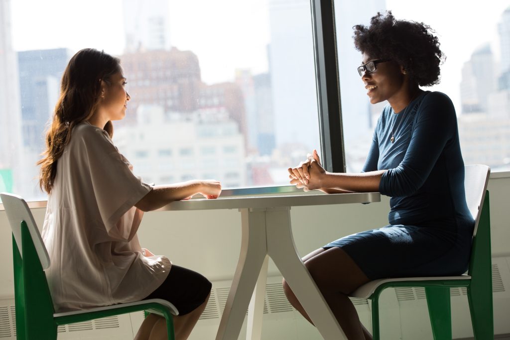 two women sit at a small table, talking.