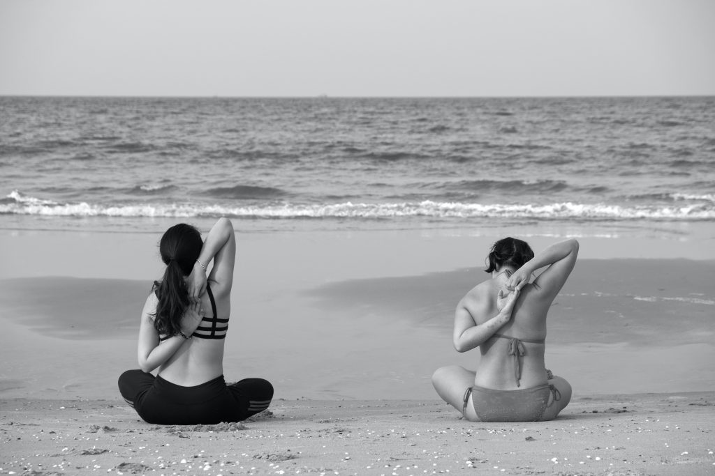two people sittig doing yoga stretched by the sea
