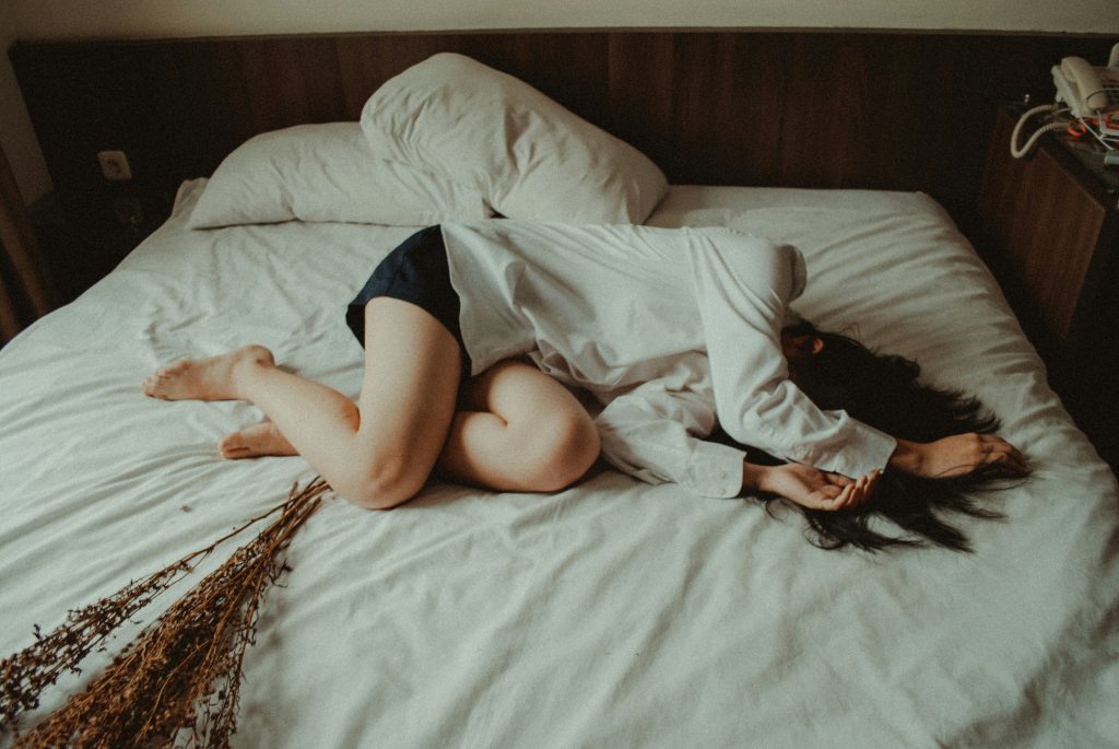 woman curled up on a bed looking as if she is in pain